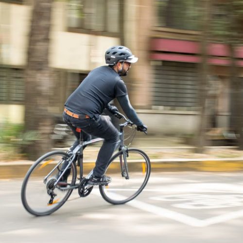 Adult male cycling on city street with helmet, promoting urban mobility.